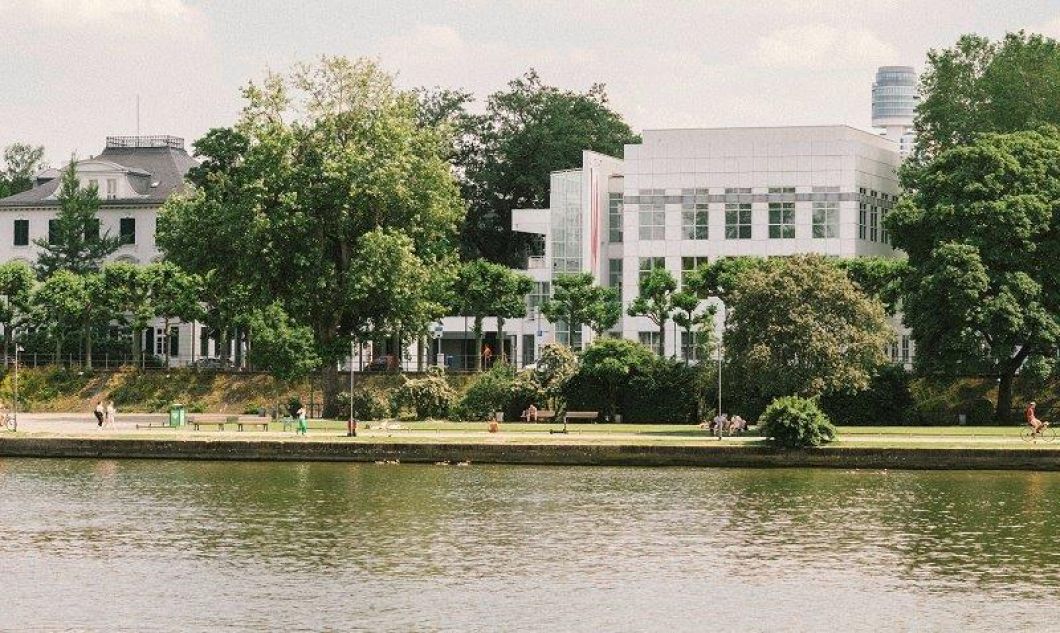 Museumsufer Frankfurt mit Museum Angewandte Kunst und Villa Metzler im Vordergrund der Fluss, einige Passanten am Ufer mit Bäumen, im Hintergrund die Museumsgebäude